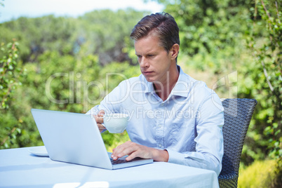 Serious businessman using laptop with coffee