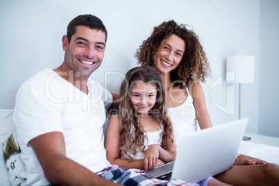 Portrait of couple using laptop with their daughter on bed