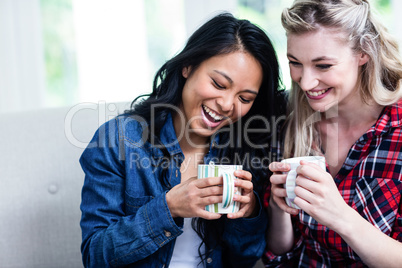 Happy young female friends drinking coffee at home