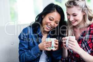 Happy young female friends drinking coffee at home