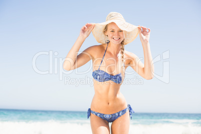Pretty woman in bikini and beach hat standing on the beach