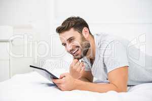 Man smiling while using digital tablet on bed