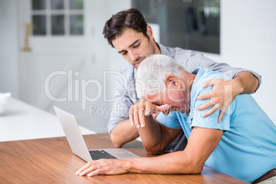 Son comforting tensed father sitting at desk