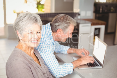 Portrait of senior woman with husband using laptop in background