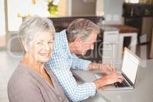Portrait of senior woman with husband using laptop in background
