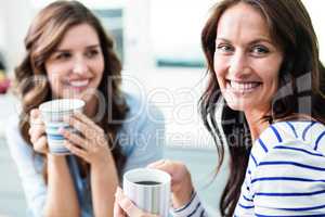 Cheerful female friends holding coffee mugs while sitting at tab