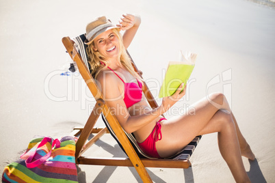Woman in bikini sitting on armchair and reading book