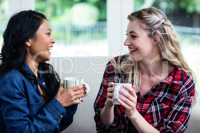 Cheerful young female friends drinking coffee at home