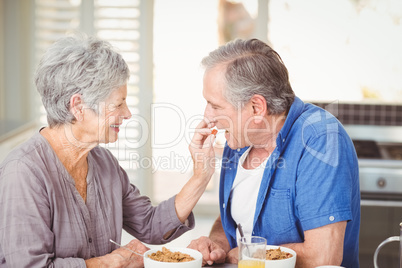 Side view of senior woman feeding husband while sitting at table