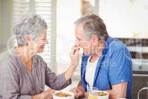 Side view of senior woman feeding husband while sitting at table