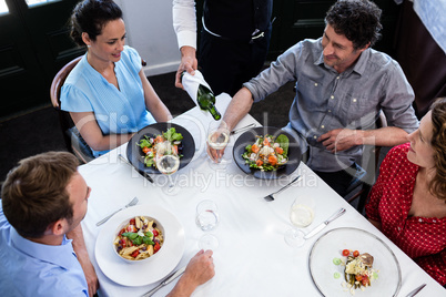 Waiter serving wine to group of friends while having lunch