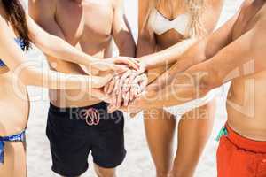 Young friends putting their hands together on the beach