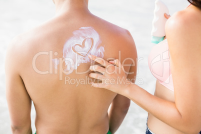 Woman making a heart symbol on mans back while applying a sunscr