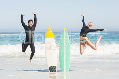 Excited couple jumping next to surfboards