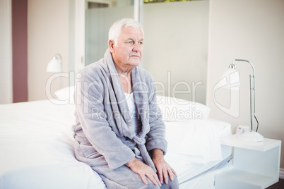 Thoughtful senior man sitting on bed