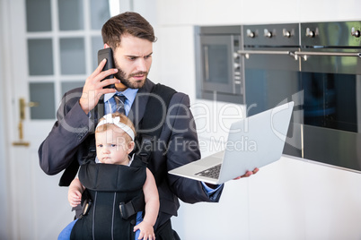 Businessman using cellphone and laptop while carrying daughter