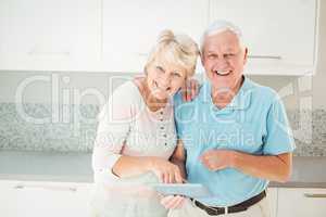 Portrait of senior couple laughing with tablet in kitchen