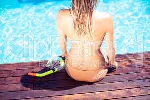 Woman sitting by swimming pool with a snorkel