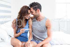 Happy young woman holding pregnancy test sitting besides husband