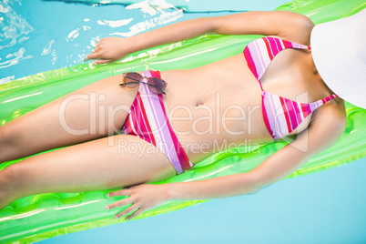 Mid section of a woman in bikini lying on air bed in swimming po