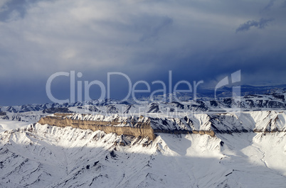 Winter mountains at sun evening and gray storm clouds