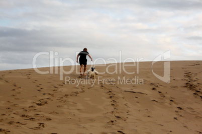 Boy Walking Dogs Up Dune