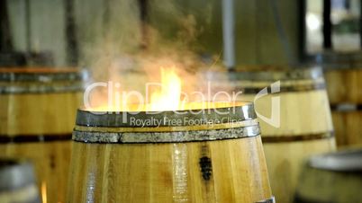 Flames rising from wood barrel and man stir the blaze for the wine barrel production.