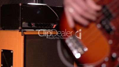 Bassist. Defocus from amplifier & speaker box in background to close-up on a male hand playing bass.