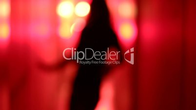 Silhouette of a sexy woman dancing in a blurry, red corridor. Medium shot.