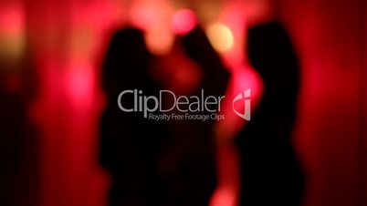 Silhouette of three sexy women dancing in a blurry, red corridor with her hands raised. Medium shot.