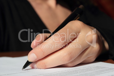 Linke Hand einer Frau unterschreibt mit Kugelschreiber Dokument