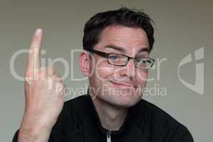 Mann mit Brille und lustigem Gesichtsausdruck zeigt mit Zeigefinger nach oben
