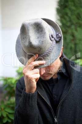 Mann senkt Kopf und hält zwei Finger an seinen Hut