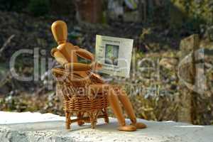 Holzfigur sitzt auf Terasse im Sessel und liest Zeitung