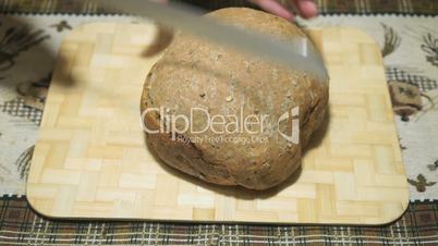 Rye-wheat bread is cut with a knife on a board