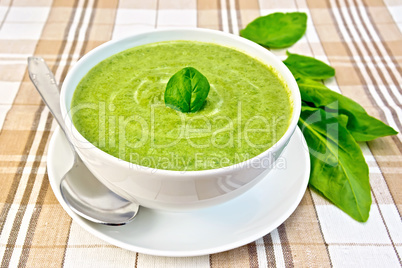 Soup puree with spinach and spoon in white bowl on fabric