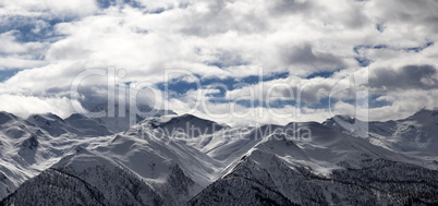 Panoramic view on snowy mountains and cloudy sky in evening