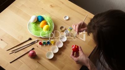 A young Woman Paints Easter Egg with a Brush on the background of Wooden Table