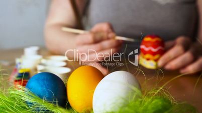 A young Woman Paints Easter Egg with a Brush on the background of Wooden Table