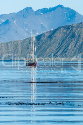 Red schooner motoring into bay past mountains