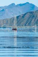 Red schooner motoring into bay past mountains