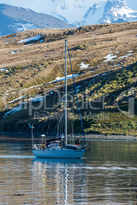 White sloop motoring past fields and mountains