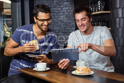 Friends using a tablet while eating sandwiches