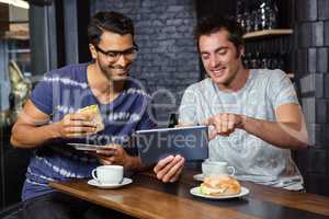 Friends using a tablet while eating sandwiches