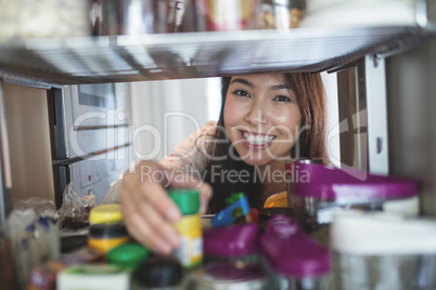 Portrait of young woman picking a bottle from storage cabinet