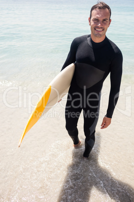 Happy surfer holding a surfboard on the beach