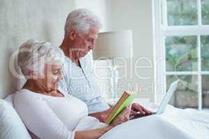 Senior woman reading book while man using laptop