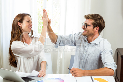 Colleagues giving high five at office desk