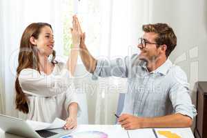 Colleagues giving high five at office desk