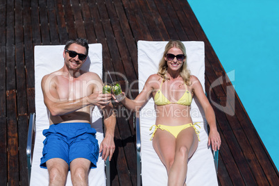 Couple sitting on sun lounger and toasting glass of mojito